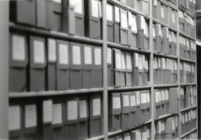 Archival boxes on shelving, black and white photo.