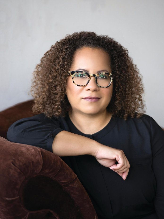 Erica Armstrong Dunbar portrait while posing on a brown couch in front of a gray background.