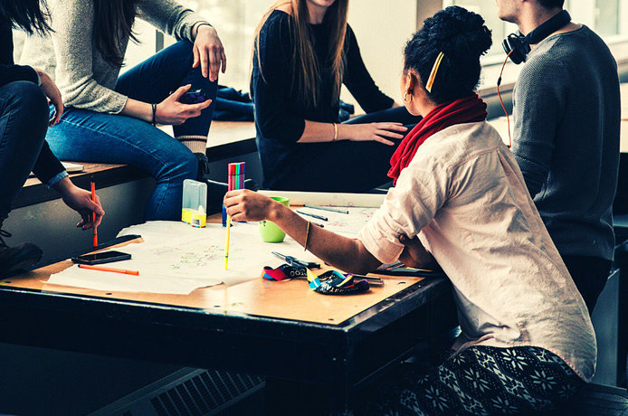 A group of students sits around a table with papers on it and participate in a focus group. 