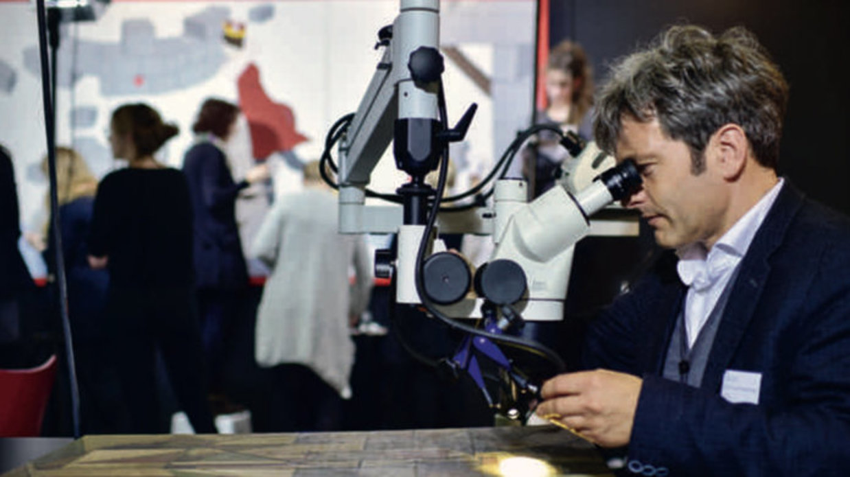 Gunnar Heydenreich observing a flat material on a table using a microscope.