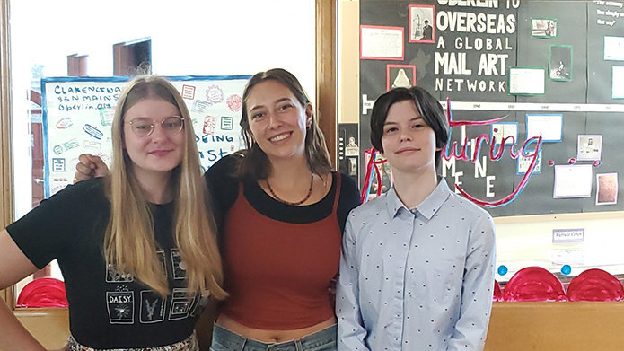 Three students posing in front of Overseas to Oberlin information board.