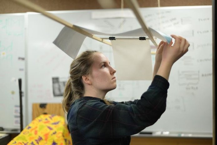 Student hanging letterpress pieces on wooden rack overhead.