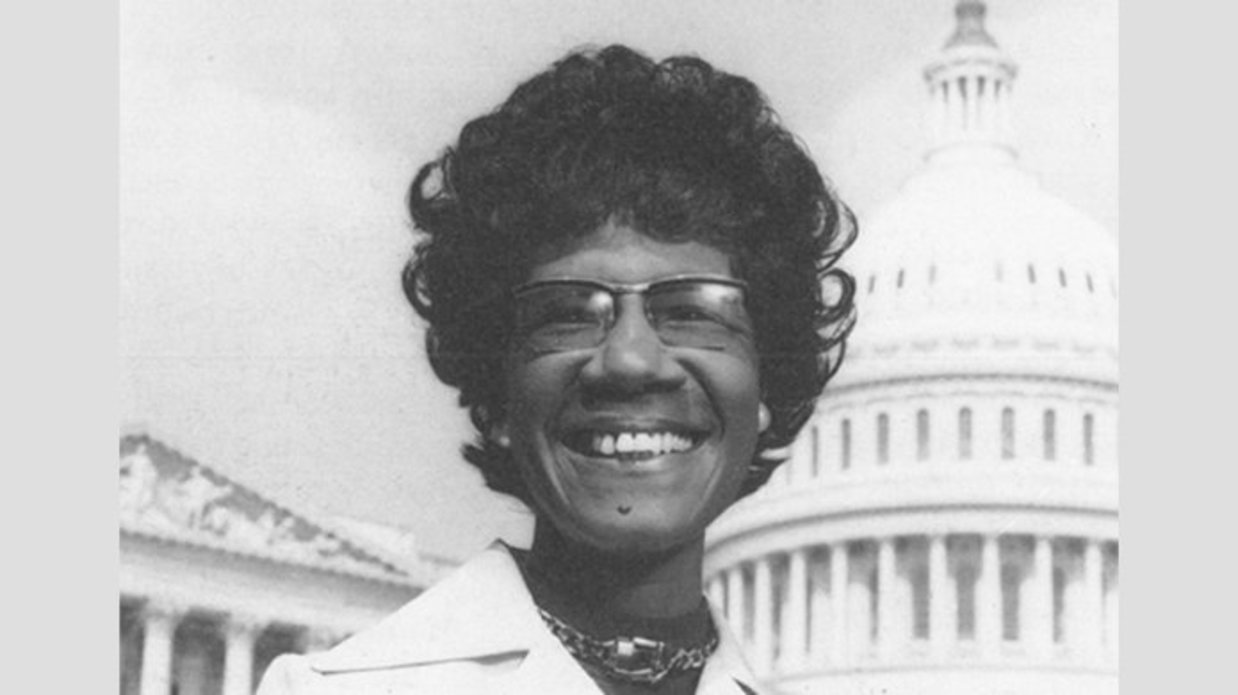 Shirley Chisholm smiling in front of the US Capitol Building, black and white photo.
