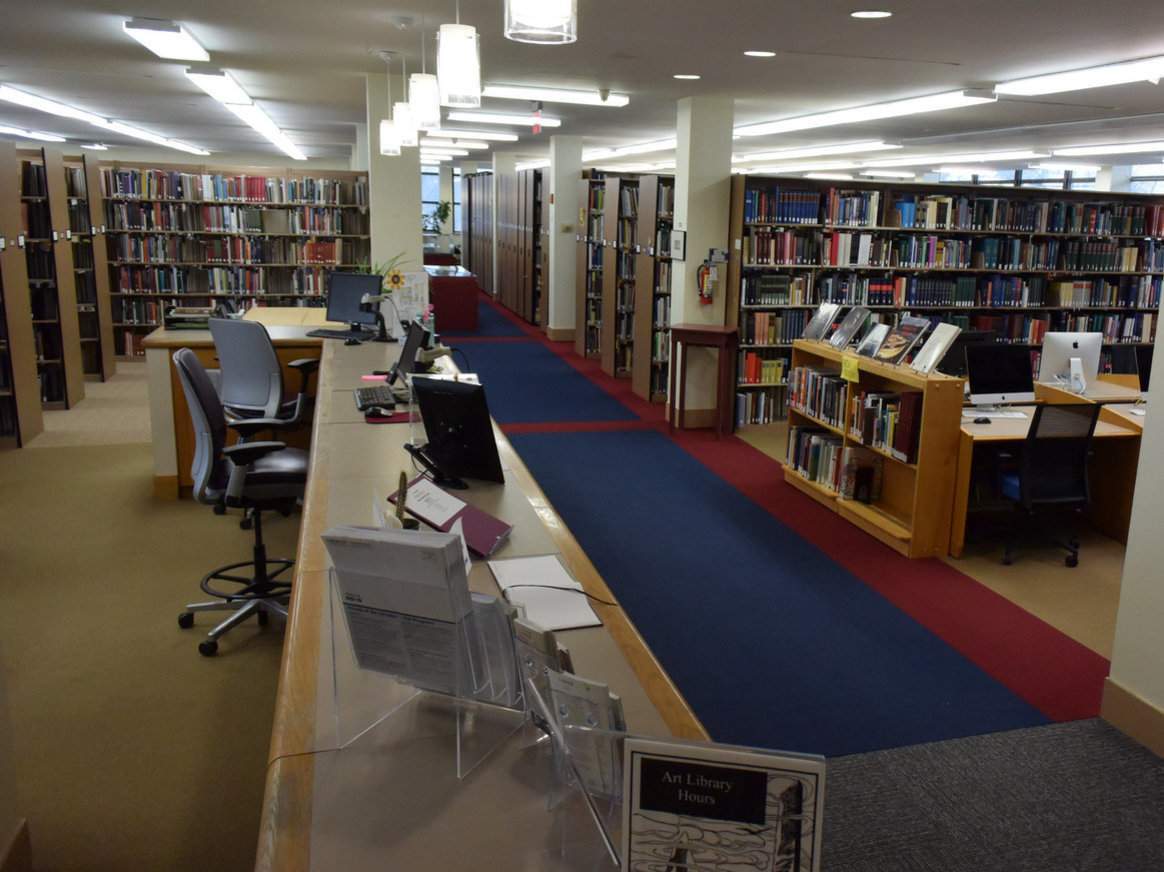 Art library view from the Circulation Desk with a view of bookshelves and the main aisle cutting between them.