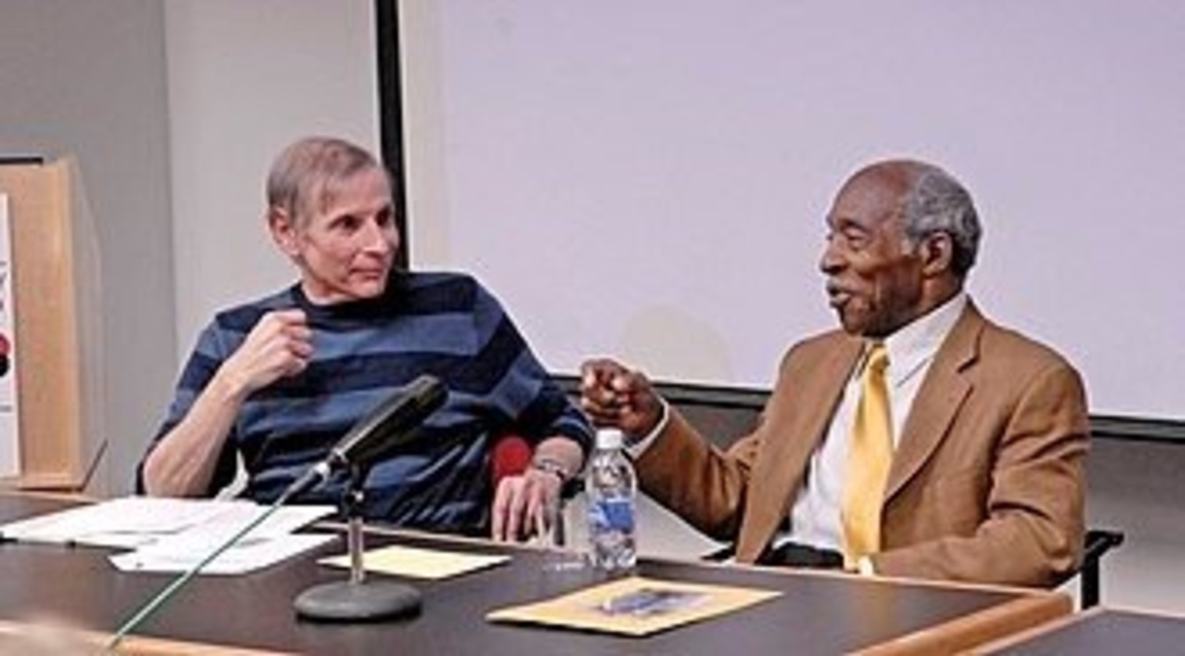 Berger sitting at a desk with Joe Wilder with a microphone in front of them.
