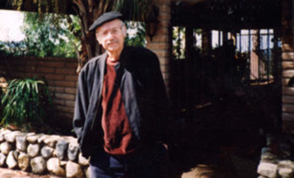 Archie Nedelman standing outside by a brick wall, tree, and low rock wall.